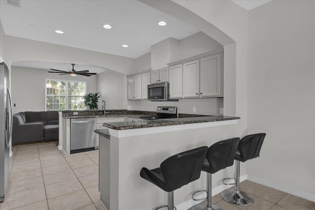 kitchen with white cabinets, kitchen peninsula, stainless steel appliances, dark stone countertops, and ceiling fan