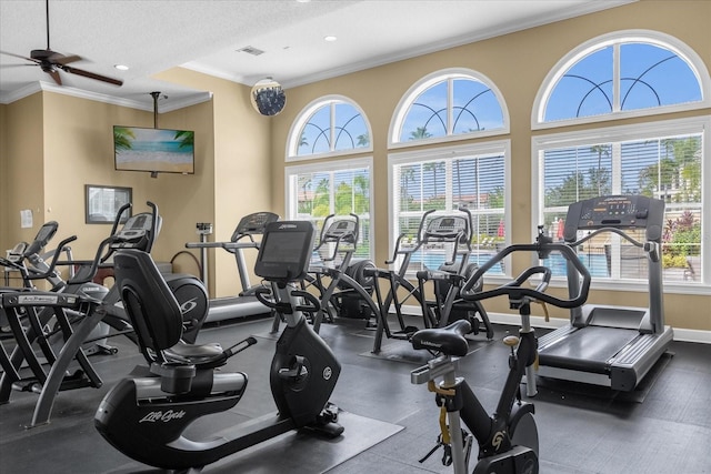 exercise room featuring ceiling fan, a textured ceiling, ornamental molding, and a high ceiling