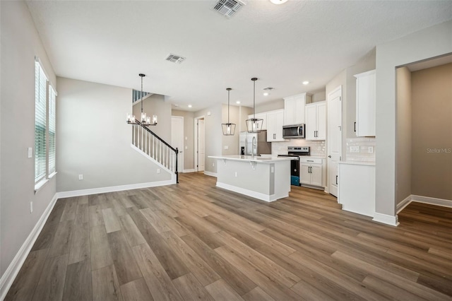 kitchen featuring hardwood / wood-style floors, white cabinets, a center island with sink, decorative light fixtures, and stainless steel appliances