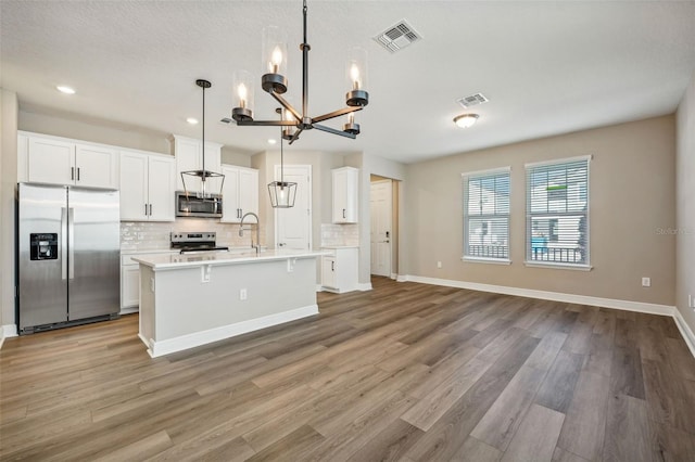 kitchen with pendant lighting, a center island with sink, light wood-type flooring, and appliances with stainless steel finishes