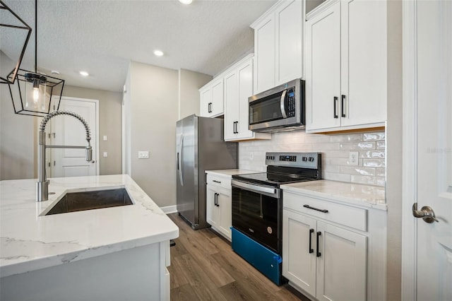 kitchen with white cabinetry, sink, stainless steel appliances, hardwood / wood-style floors, and pendant lighting