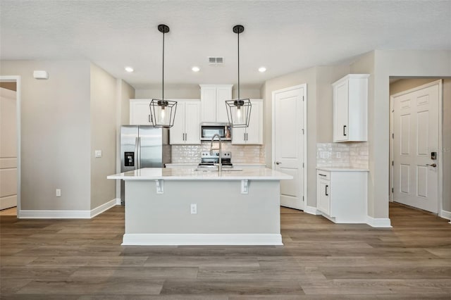 kitchen featuring hardwood / wood-style floors, a center island with sink, white cabinets, hanging light fixtures, and stainless steel appliances