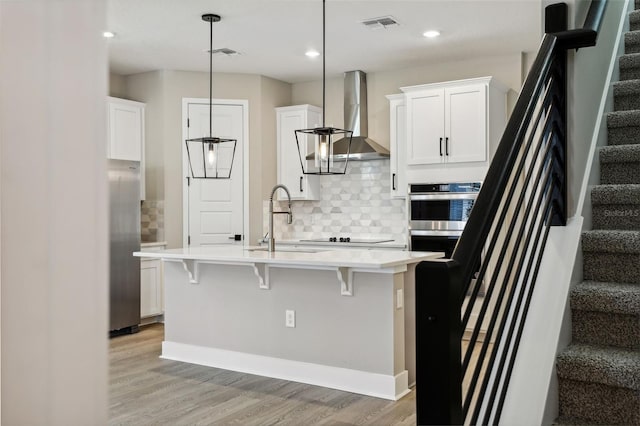 kitchen featuring white cabinetry, sink, wall chimney exhaust hood, hanging light fixtures, and a breakfast bar