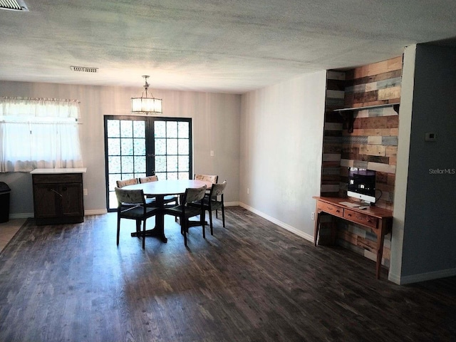 dining space featuring dark wood-type flooring, wood walls, a textured ceiling, and a chandelier