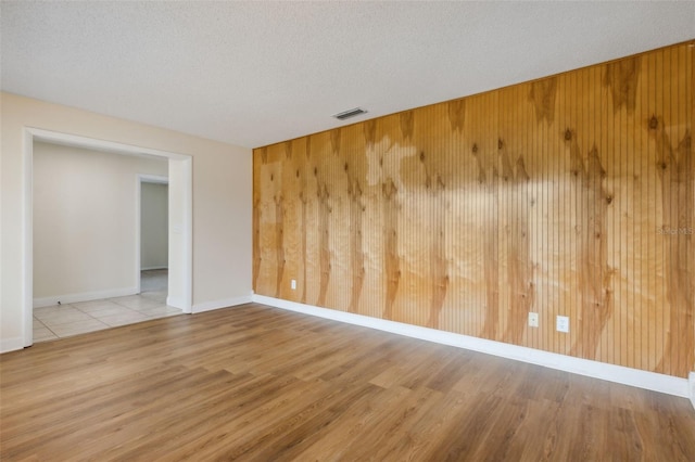 empty room with wood walls, a textured ceiling, and light hardwood / wood-style flooring