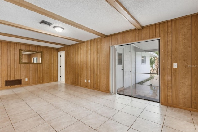 empty room featuring beam ceiling, wooden walls, and a textured ceiling