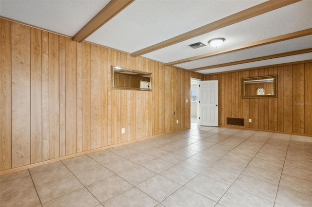 spare room with beam ceiling, wooden walls, and a textured ceiling