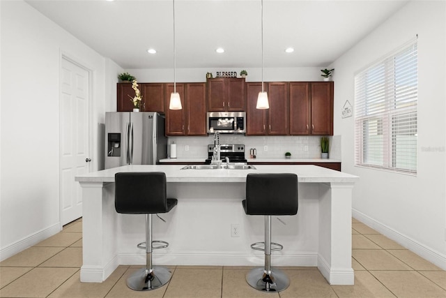 kitchen with an island with sink, decorative light fixtures, stainless steel appliances, a kitchen breakfast bar, and decorative backsplash