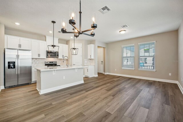 kitchen featuring pendant lighting, a kitchen island with sink, appliances with stainless steel finishes, and light hardwood / wood-style flooring