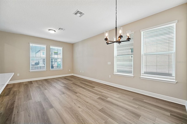 unfurnished dining area with a textured ceiling, light hardwood / wood-style flooring, and a notable chandelier