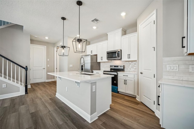 kitchen with a kitchen island with sink, pendant lighting, white cabinets, and stainless steel appliances