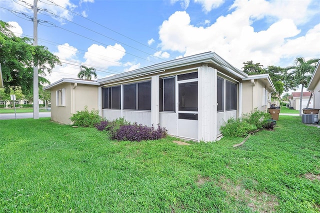 view of side of home with cooling unit, a sunroom, and a yard