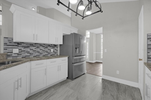kitchen featuring white cabinets, stainless steel refrigerator with ice dispenser, baseboards, and backsplash