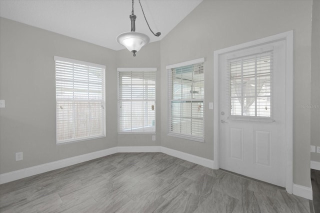 unfurnished dining area featuring lofted ceiling, a wealth of natural light, and baseboards