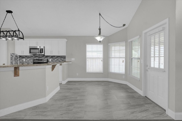 kitchen with stainless steel appliances, backsplash, vaulted ceiling, a kitchen bar, and white cabinetry