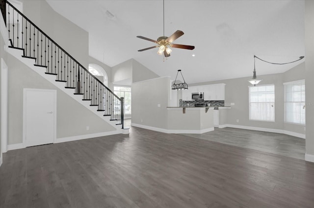 unfurnished living room featuring dark wood-style floors, baseboards, stairway, ceiling fan, and high vaulted ceiling
