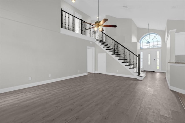 unfurnished living room with a towering ceiling, ceiling fan, and dark wood-type flooring