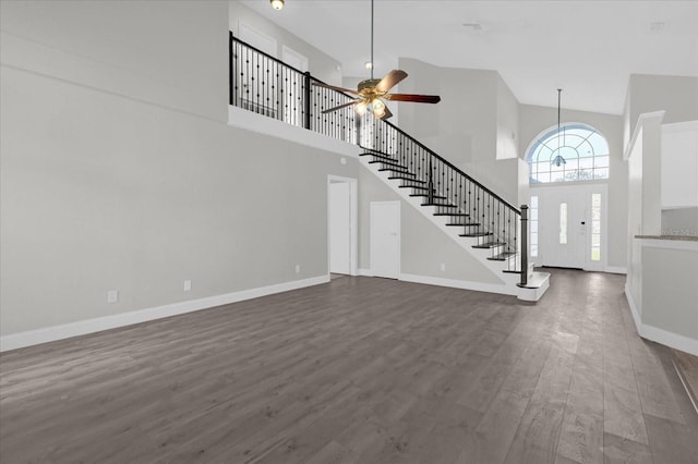 unfurnished living room with stairs, ceiling fan, baseboards, a high ceiling, and dark wood-type flooring