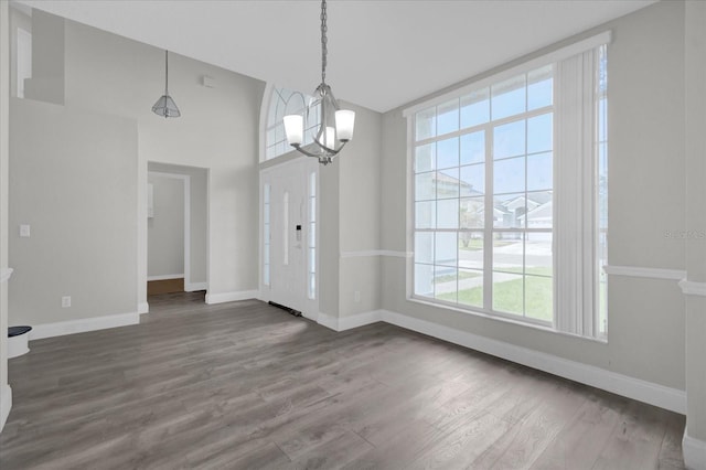 unfurnished dining area with lofted ceiling, wood-type flooring, a chandelier, and plenty of natural light