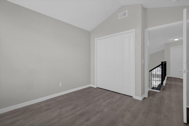 unfurnished bedroom featuring vaulted ceiling, wood finished floors, a closet, baseboards, and visible vents