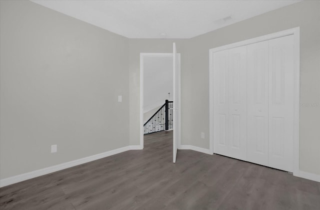 unfurnished bedroom with baseboards, wood finished floors, visible vents, and a closet