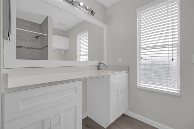 full bath with wood finished floors, baseboards, vanity, and tiled shower