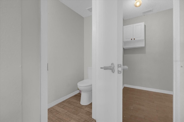bathroom with a textured ceiling, wood finished floors, baseboards, toilet, and visible vents