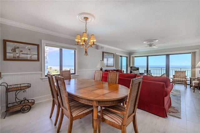 dining room featuring a textured ceiling, ceiling fan with notable chandelier, a water view, and crown molding