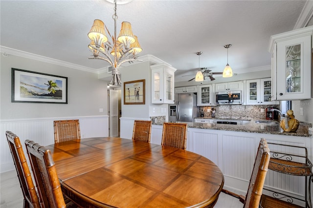 dining room with a textured ceiling, sink, ceiling fan with notable chandelier, wooden walls, and crown molding