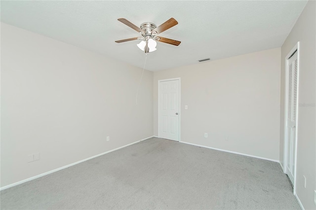 unfurnished bedroom with a textured ceiling, a closet, light colored carpet, and ceiling fan