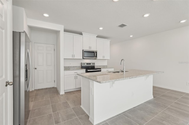 kitchen featuring appliances with stainless steel finishes, white cabinetry, sink, light stone countertops, and a center island with sink