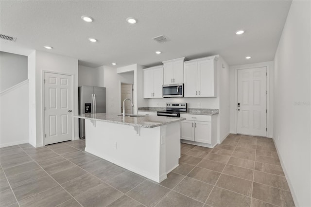 kitchen featuring sink, a center island with sink, appliances with stainless steel finishes, light stone countertops, and white cabinets