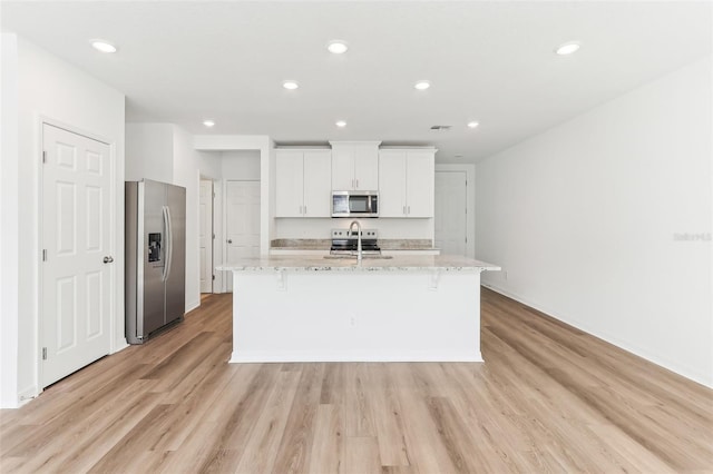 kitchen featuring appliances with stainless steel finishes, light stone countertops, a center island with sink, and white cabinets