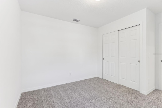 unfurnished bedroom with light colored carpet, a closet, and a textured ceiling