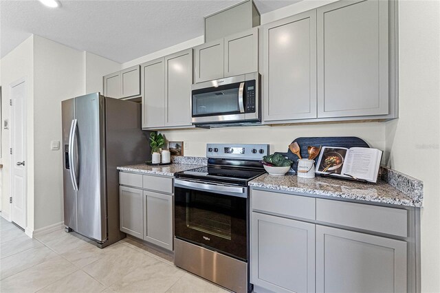 kitchen with light stone counters, light tile patterned flooring, gray cabinetry, a textured ceiling, and appliances with stainless steel finishes