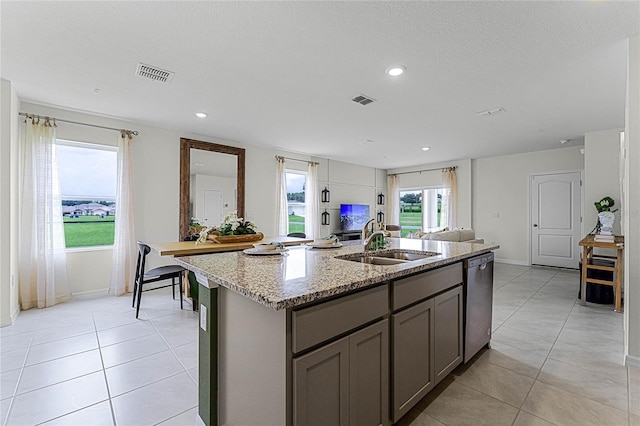 kitchen with light stone counters, dishwasher, light tile patterned floors, a center island with sink, and sink