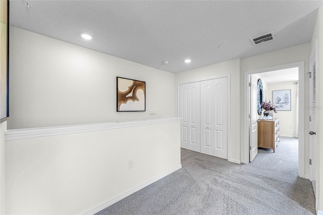 hall with light carpet and a textured ceiling