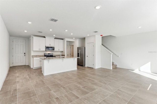 kitchen featuring light tile patterned floors, appliances with stainless steel finishes, light stone counters, white cabinets, and a center island with sink