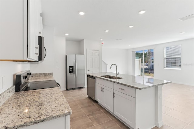 kitchen featuring sink, appliances with stainless steel finishes, white cabinetry, light stone countertops, and an island with sink