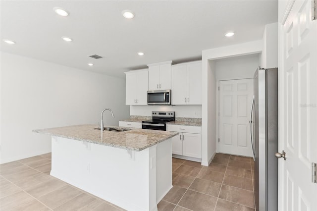 kitchen with sink, appliances with stainless steel finishes, light stone counters, white cabinets, and a center island with sink