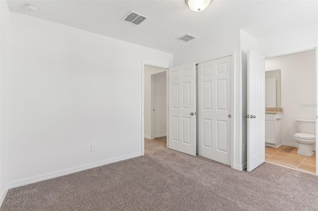 unfurnished bedroom with light colored carpet, ensuite bath, and a closet