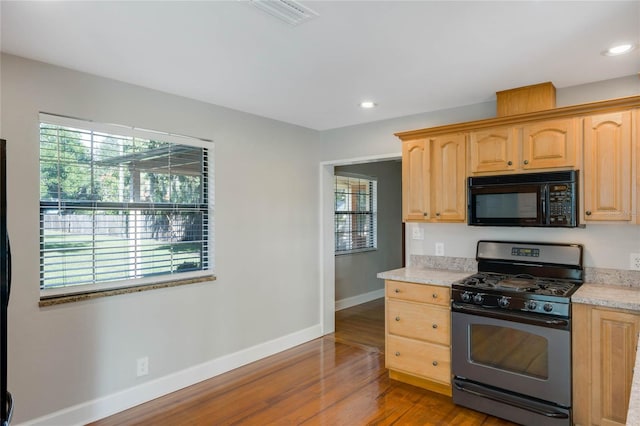 kitchen featuring stainless steel gas stove, light brown cabinetry, and hardwood / wood-style floors