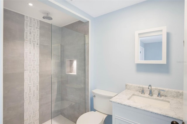 bathroom with a tile shower, vanity, and toilet