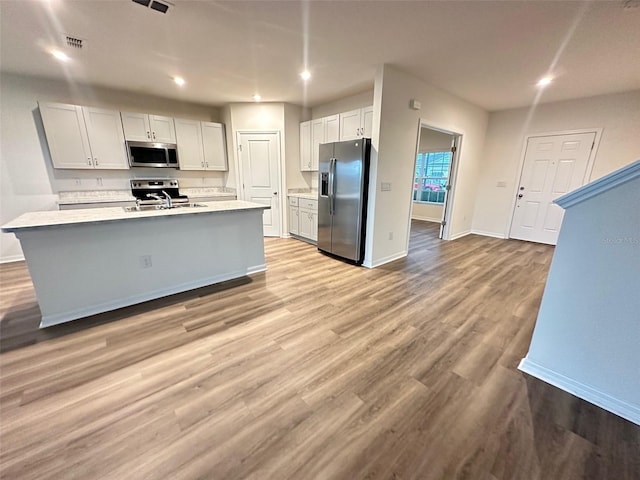 kitchen with white cabinets, an island with sink, stainless steel appliances, and light hardwood / wood-style floors