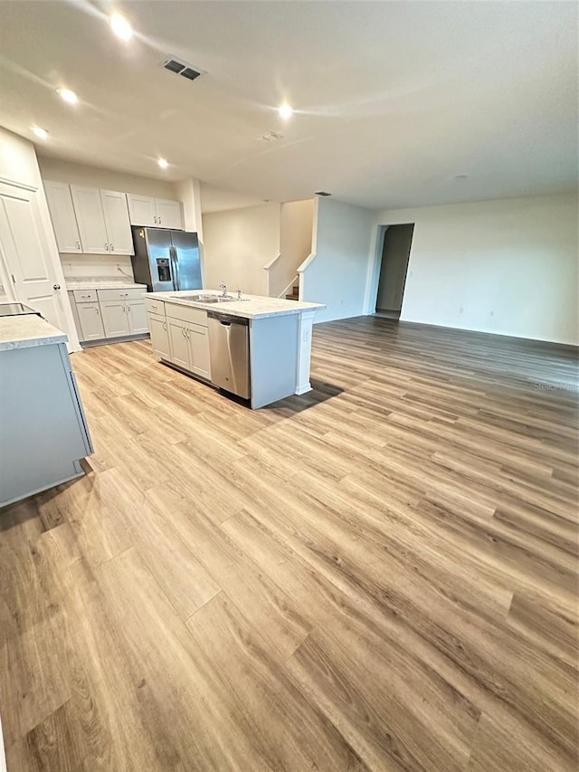 kitchen featuring stainless steel appliances, light wood-style floors, a center island with sink, light countertops, and open floor plan