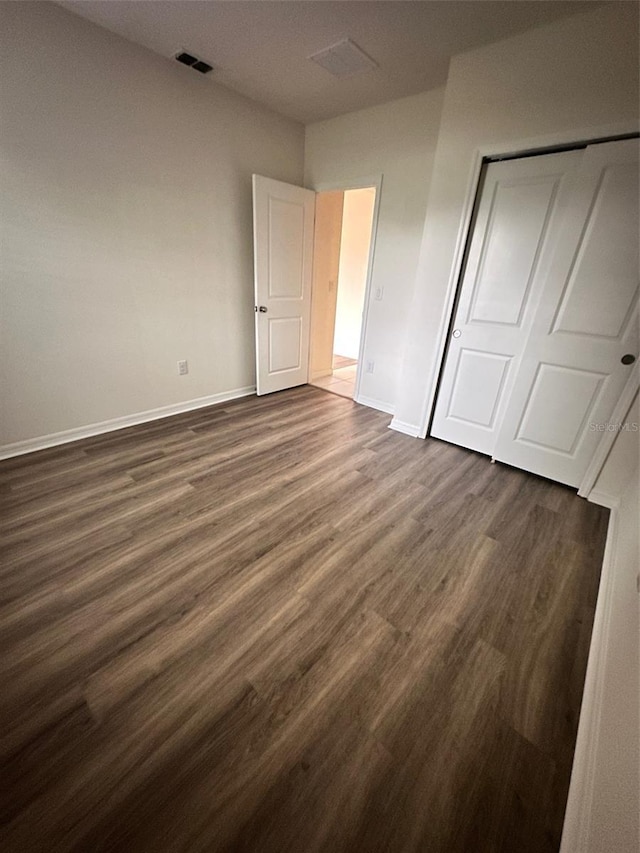 unfurnished bedroom with baseboards, visible vents, dark wood-style flooring, and a closet