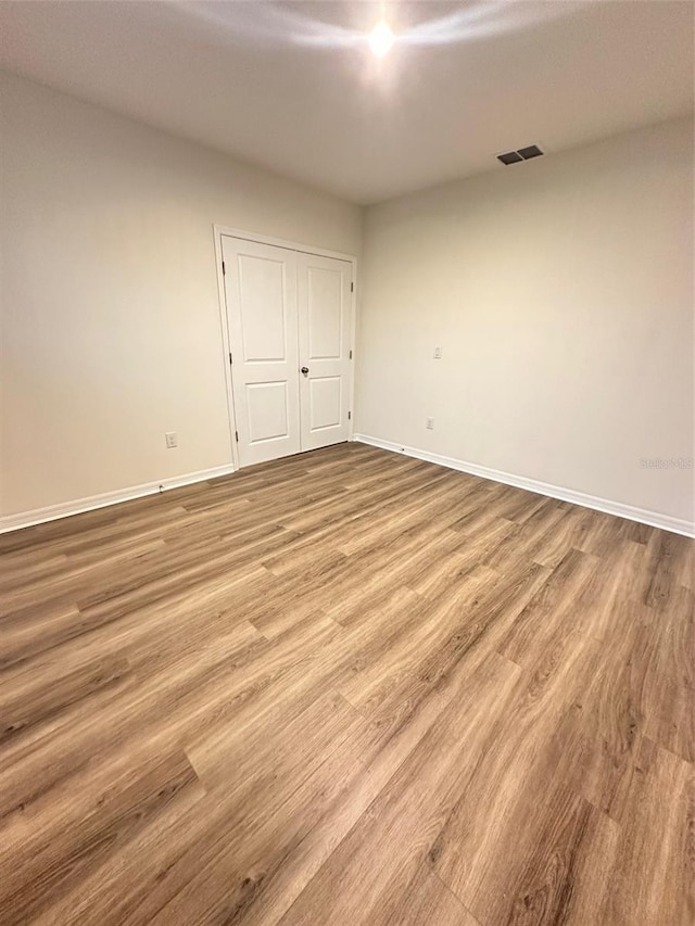 empty room with wood finished floors, visible vents, and baseboards