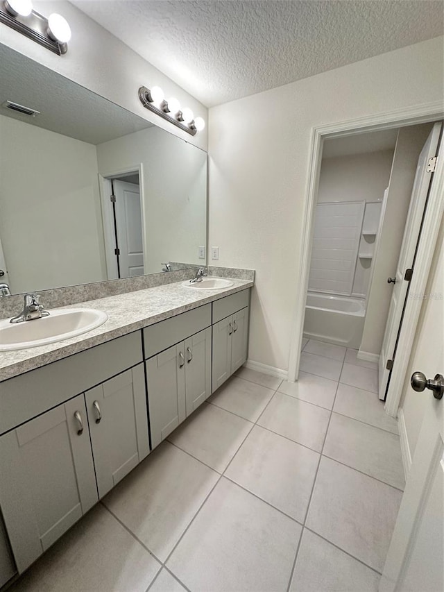 bathroom with tile patterned floors, a textured ceiling, double vanity, and a sink