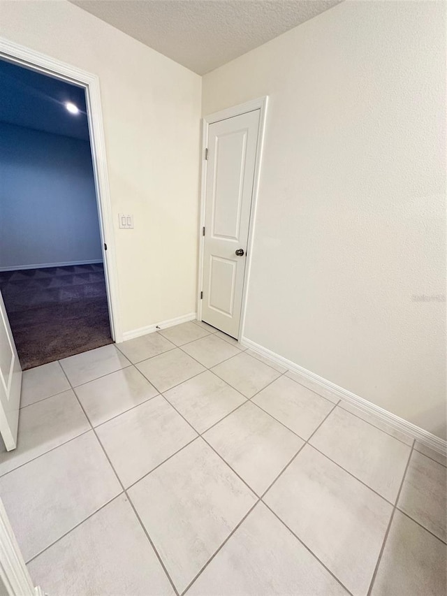 empty room with light tile patterned flooring, baseboards, and a textured ceiling