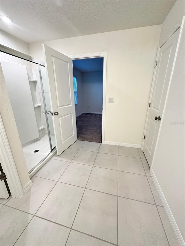 bathroom with tile patterned floors, a shower stall, a textured ceiling, and baseboards